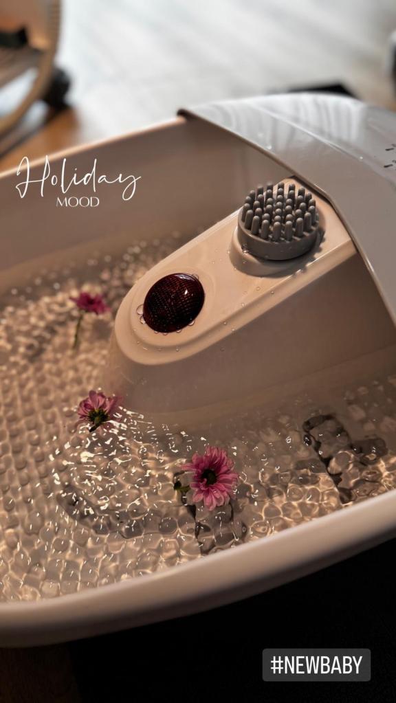Nahaufnahme eines Fußbades mit Wasser, dekoriert mit kleinen Blüten und einem Massageroller.
